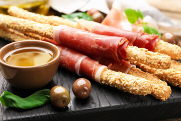 Grissini breadsticks with prosciutto, olives and honey on wooden table, closeup