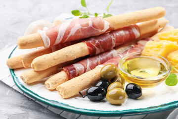 Grissini breadsticks with prosciutto, cheese, olives and honey on grey table, closeup