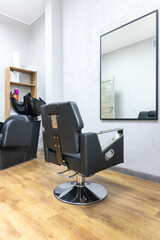 Empty black barber chair in front of wall mirror in hair salon interior.