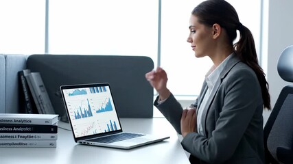 Businesswoman Analyzing Financial Graphs on Laptop - A young businesswoman sits at her desk, reviewing financial data displayed as graphs on her laptop. - Powered by Adobe