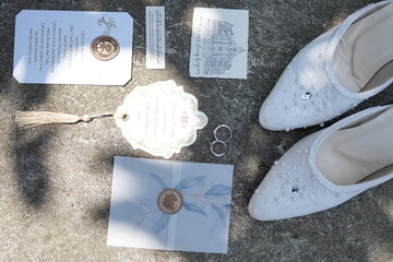 Elegant wedding flat lay with bridal shoes, rings, and invitations on a textured stone background
