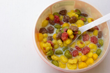 A bowl of colorful cereals with milk isolated on white background.
