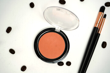 Open blush compact with makeup brushes and scattered coffee beans on white background, stylish flat...