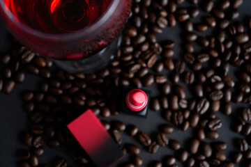 Red lipstick placed among roasted coffee beans with glass of wine above, stylish top view composition blending beauty, elegance and lifestyle mood.