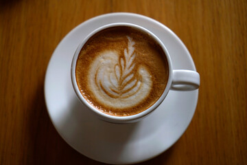 Hot cappuccino in white cup with delicate latte art on wooden table, minimal cafe atmosphere, warm tones and cozy coffee break moment