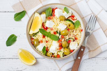 A bright, fresh salad with couscous, feta cheese, vegetables, and herbs on a light background. A healthy and delicious concept, a vegetarian dish for lunch or dinner.