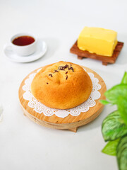 Golden baked bun with chocolate sprinkles topping served on wooden tray with butter and tea