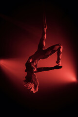Female aerialist performs an inverted backbend on straps, body arched with legs extended, gripping...