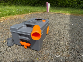 A portable toilet cassette from a motorhome or caravan is sat on gravel pitch drying after being cleaned 