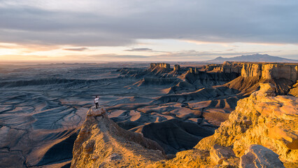 Adventurous picture of traveler explorer standing on rock looking into the vast distant landscape. Golden light during morning sunrise at Moonscape overlook in Utah, USA. 