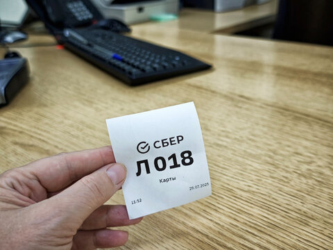Kirov, Russia - July 29, 2025: Holding a queue number at Sberbank while waiting in line for banking services