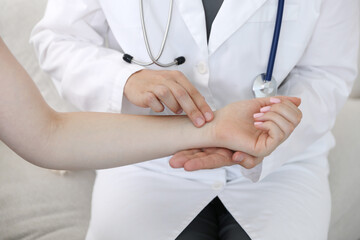 Doctor checking woman's pulse with fingers indoors, closeup