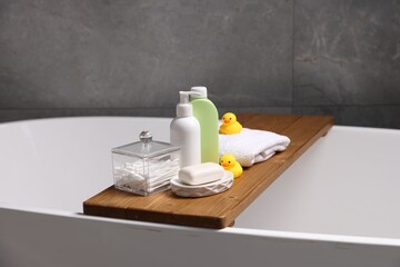 Baby accessories and bathing products on wooden tray in bathtub indoors, closeup