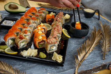 Philadelphia sushi set on a large black tray with soy sauce and a girl's hands with chopsticks holding a roll