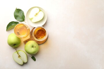 Fresh cider in glasses, apples and green leaves on beige table, flat lay. Space for text