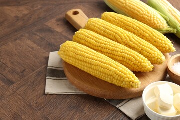 Tasty boiled corncobs and butter on wooden table, closeup