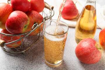 Pouring delicious cider into glass at light grey table, closeup