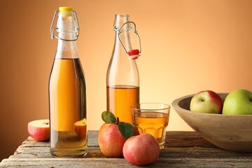 Delicious cider in bottles, glass and apples on wooden table against orange gradient background