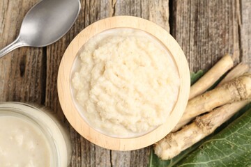 Tasty horseradish sauce, spoon and roots on wooden table, flat lay