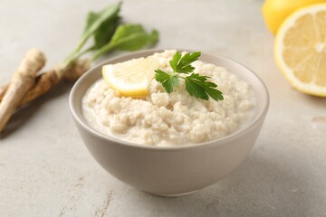 Tasty horseradish sauce with parsley, lemon slice and roots on light table, closeup