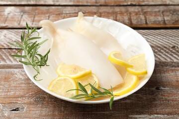 Pieces of raw squids with ice cubes, rosemary and lemon on color wooden table, closeup