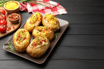 Tasty stuffed baked potatoes on black wooden table, space for text