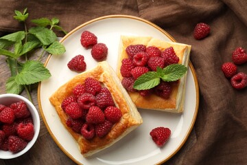 Yummy puff pastries with raspberries and mint on wooden table, flat lay