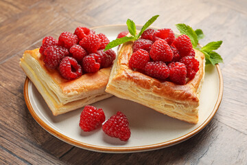 Yummy puff pastries with raspberries and mint on wooden table, closeup