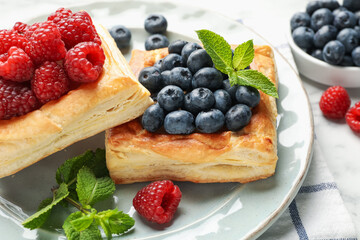 Yummy puff pastries with berries and mint on white table, closeup