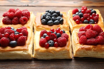 Tasty puff pastries with berries on wooden table, closeup