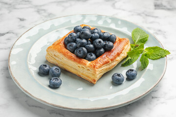 Tasty puff pastry with blueberries and mint on white marble table, closeup