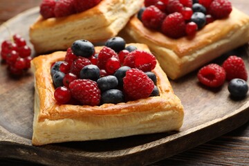Tasty puff pastries with berries on wooden table, closeup