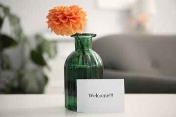 Card with word Welcome and vase with flower on white table indoors