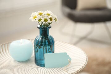 Blank card, vase with flowers and candle on table indoors. Space for text