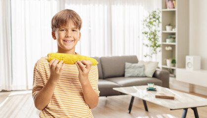 Boy standing in a room and eating corn
