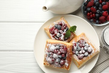 Tasty puff pastries with berries, powdered sugar and mint on white wooden table, flat lay. Space for text