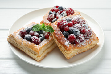 Tasty puff pastries with berries, powdered sugar and mint on white wooden table, closeup