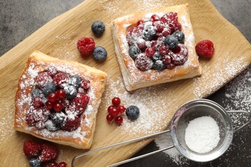 Tasty puff pastries with berries and powdered sugar on grey table, top view