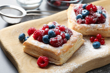 Tasty puff pastries with berries and powdered sugar on table, closeup
