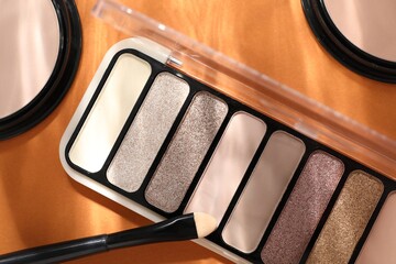 Colorful eyeshadow palette, powders and makeup applicator on orange background with shadows, flat lay