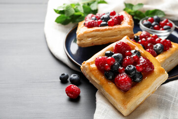 Tasty puff pastries with berries and mint on grey wooden table, closeup. Space for text