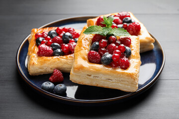 Tasty puff pastries with berries and mint on grey wooden table, closeup