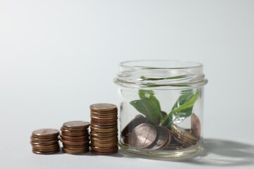 Glass jar with coins and sprout on light grey background, closeup