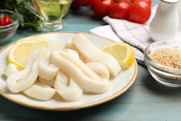 Raw squid rings, lemon and spices on light blue wooden table, closeup