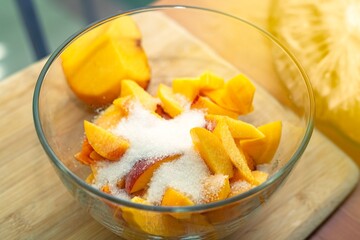Sliced ripe apricots mixed with sugar for homemade jam preparation in a glass bowl on a kitchen table