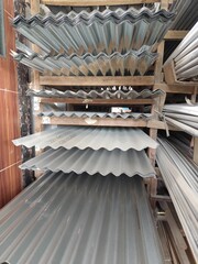 A stack of corrugated metal roofing sheets displayed on wooden racks in a hardware store. The galvanized steel sheets are arranged neatly in layers.