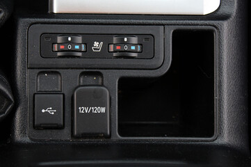Close-up of black plastic car control panel with two round seat ventilation and heating dials, USB port, and 12V, 120W socket, combining comfort and modern design.