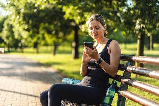Woman, smile and phone on run, nature and digital by message, notification. Happy person, trail and exercise for fitness, sportswear and sweat in outdoors, workout and health by cardio, break and fit. - Powered by Adobe