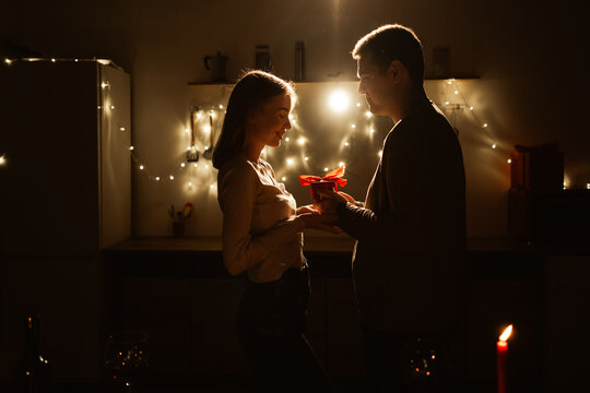 Passionate young couple sharing present on a romantic date at night in the kitchen. Celebration of Valentines day