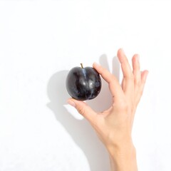 Hand holding a dark plum against white background